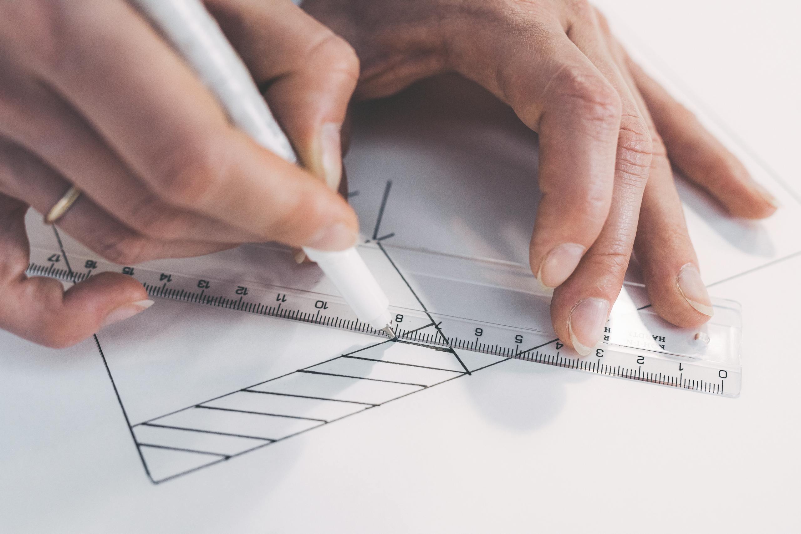 Close-up of hands drawing precise lines with ruler and pen, emphasizing accuracy.